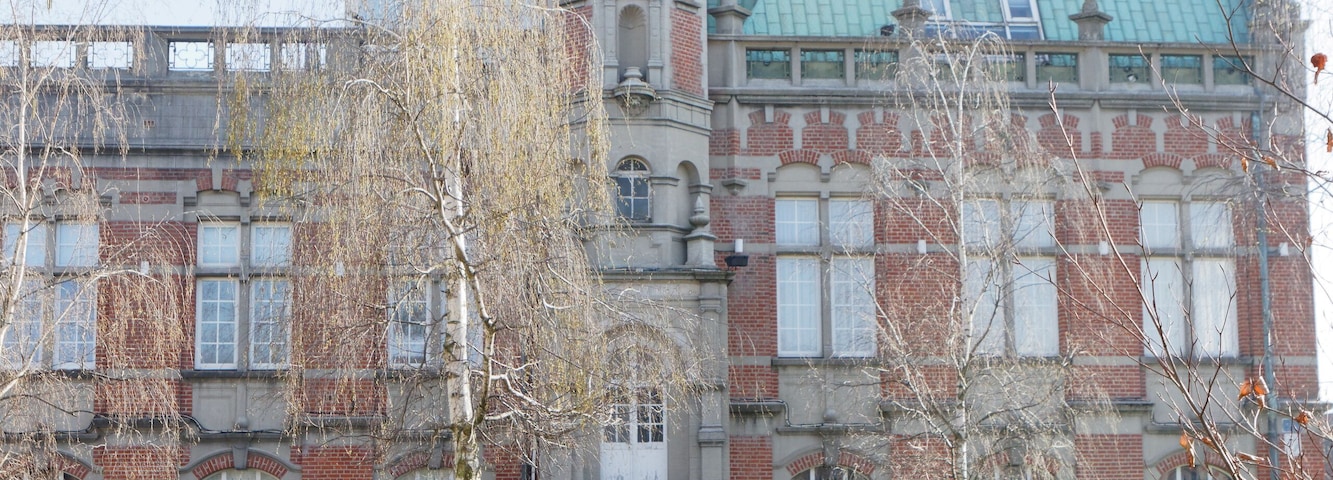 Un edificio histórico con una torre de reloj, rodeado por un jardín bien cuidado con flores de colores.