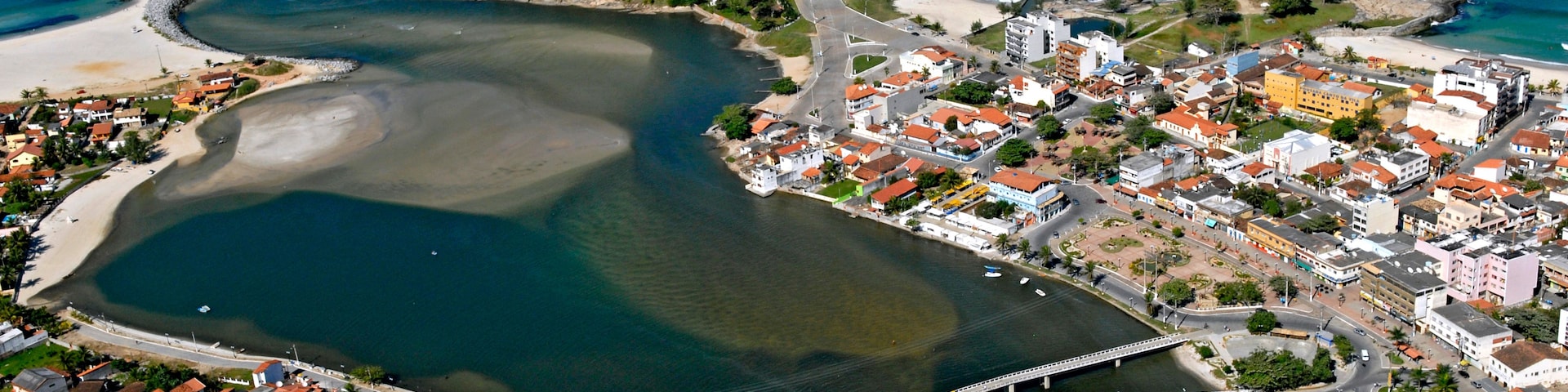 Vista aérea de uma cidade costeira com uma igreja branca imponente, uma ponte e uma combinação de edifícios residenciais e comerciais.