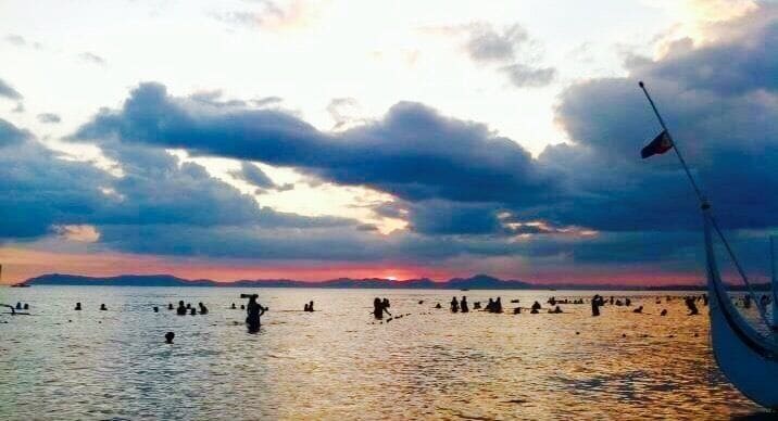 A sunset over a body of water with a boat and people in the distance.