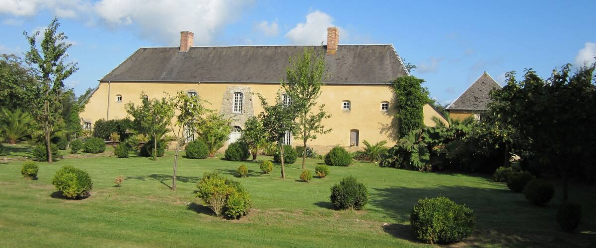 A large yellow building with a grey roof, surrounded by a well-maintained lawn and various trees.