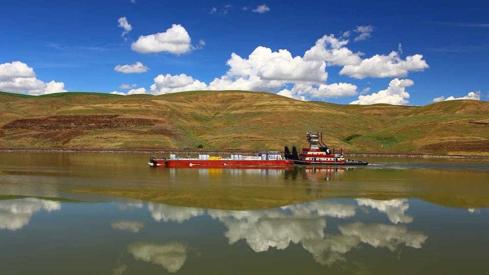 A red tugboat on a calm lake with hills in the background.
