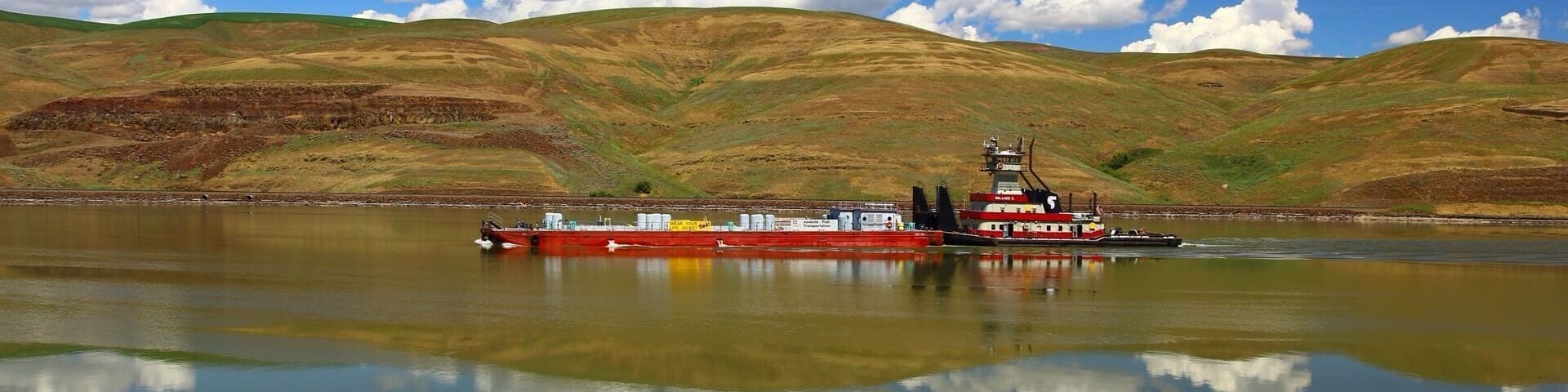 A red tugboat on a calm lake with hills in the background.