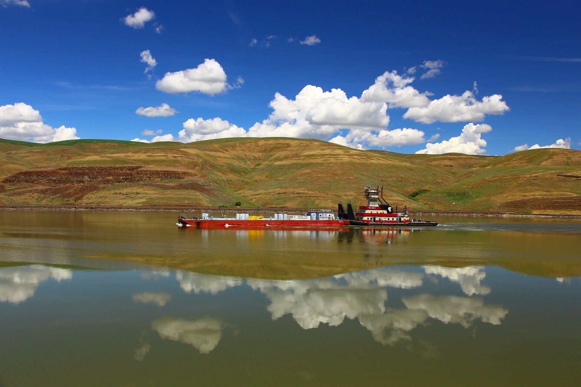 A red tugboat on a calm lake with hills in the background.