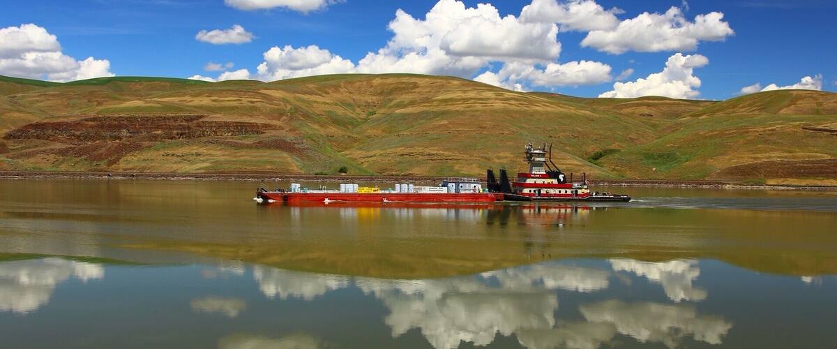 A red tugboat on a calm lake with hills in the background.