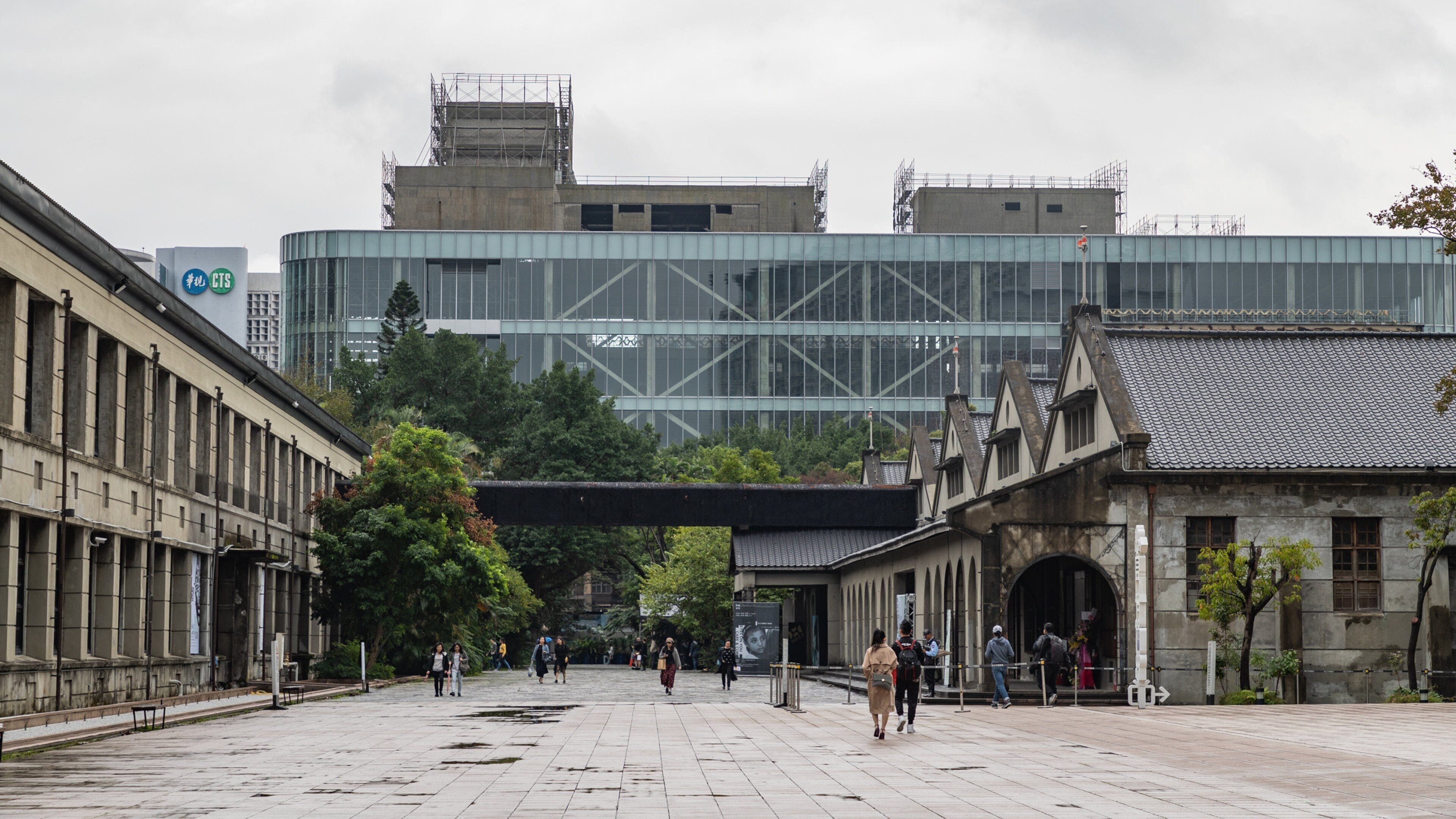 A city square with historic buildings, a modern glass structure, and pedestrians.