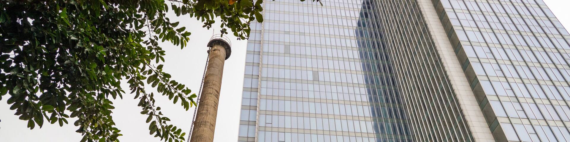 Un edificio histórico con una chimenea alta, rodeado de rascacielos modernos.