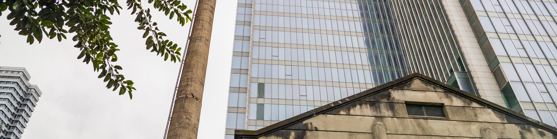 Um edifício histórico com uma chaminé alta, rodeado por arranha-céus modernos.