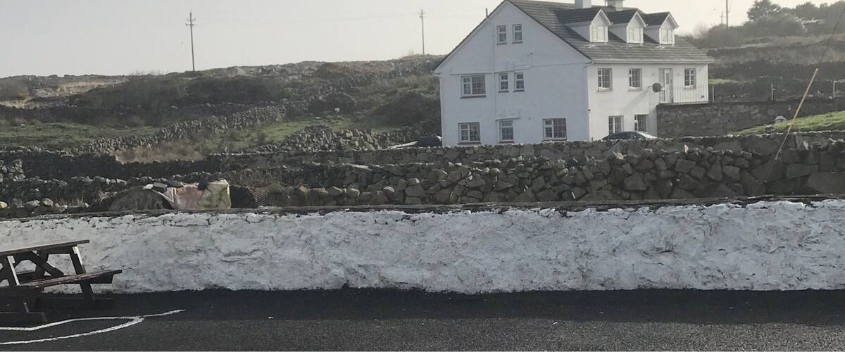 A white house with a stone wall in the foreground and a rocky hill in the background.