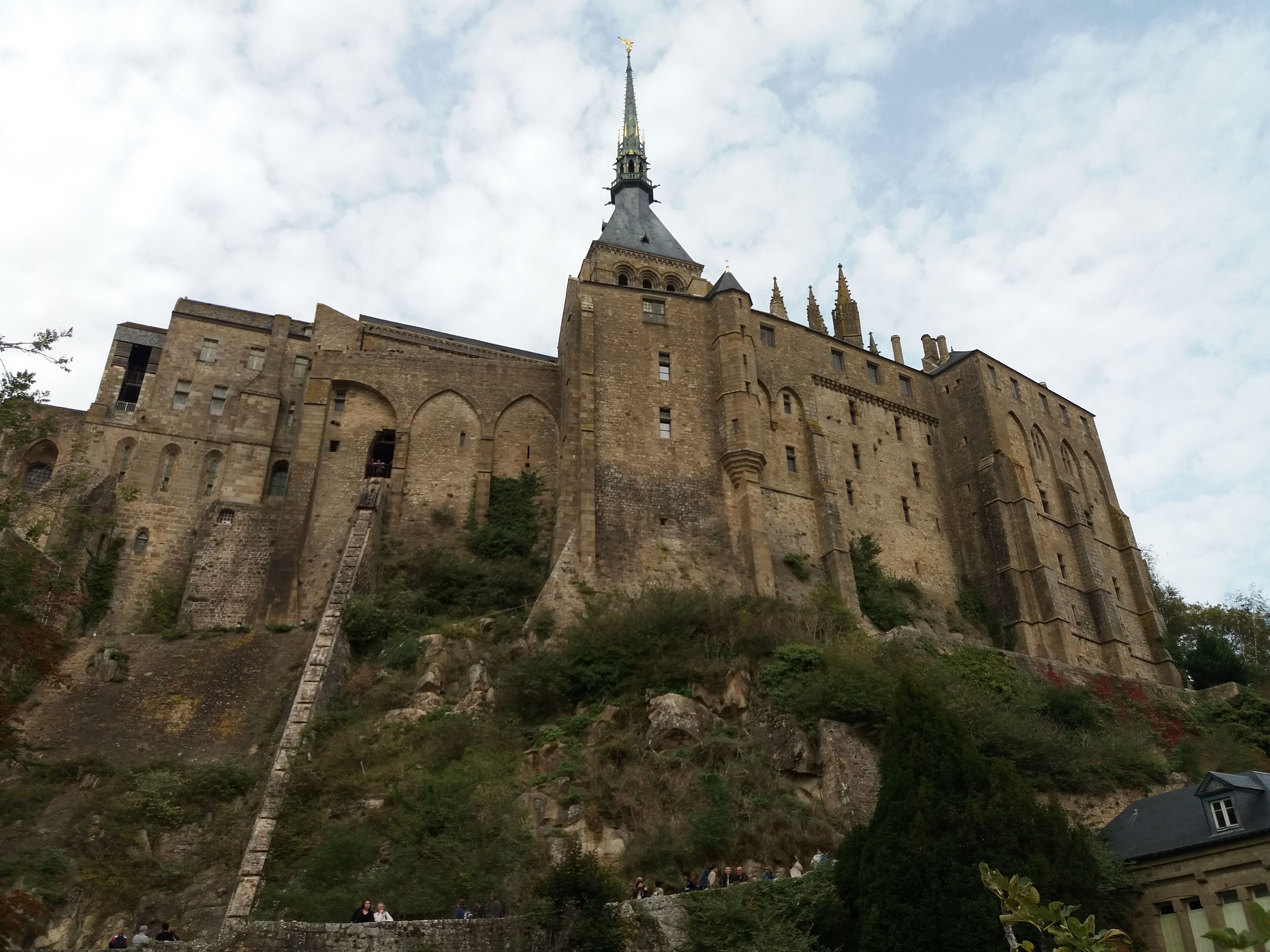 A large, historic castle with multiple towers and a prominent spire, situated on a hill with a stone staircase leading up to it.