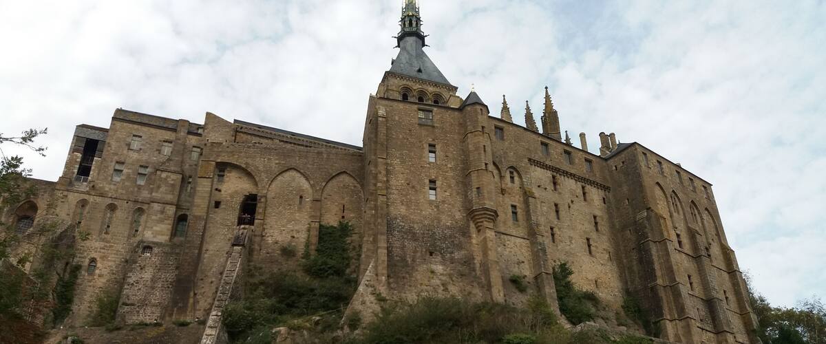 A large, historic castle with multiple towers and a prominent spire, situated on a hill with a stone staircase leading up to it.