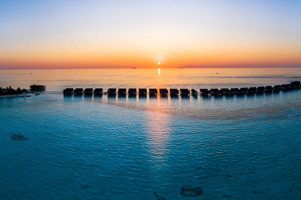 A sunset over a calm sea with overwater bungalows and a pier.