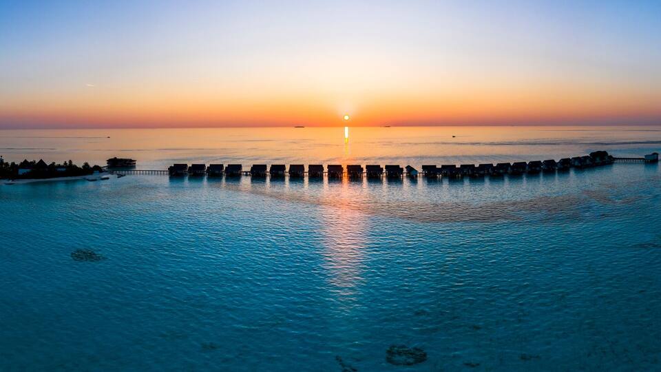 A sunset over a calm sea with overwater bungalows and a pier.