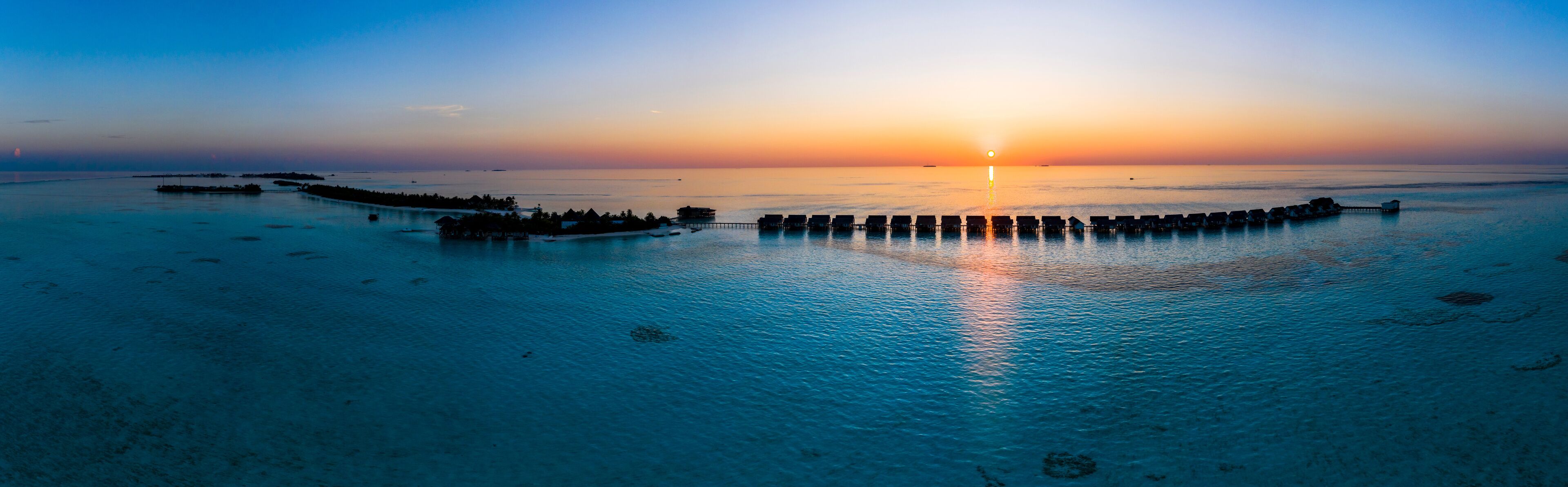 A sunset over a calm sea with overwater bungalows and a pier.