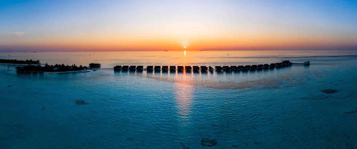 A sunset over a calm sea with overwater bungalows and a pier.