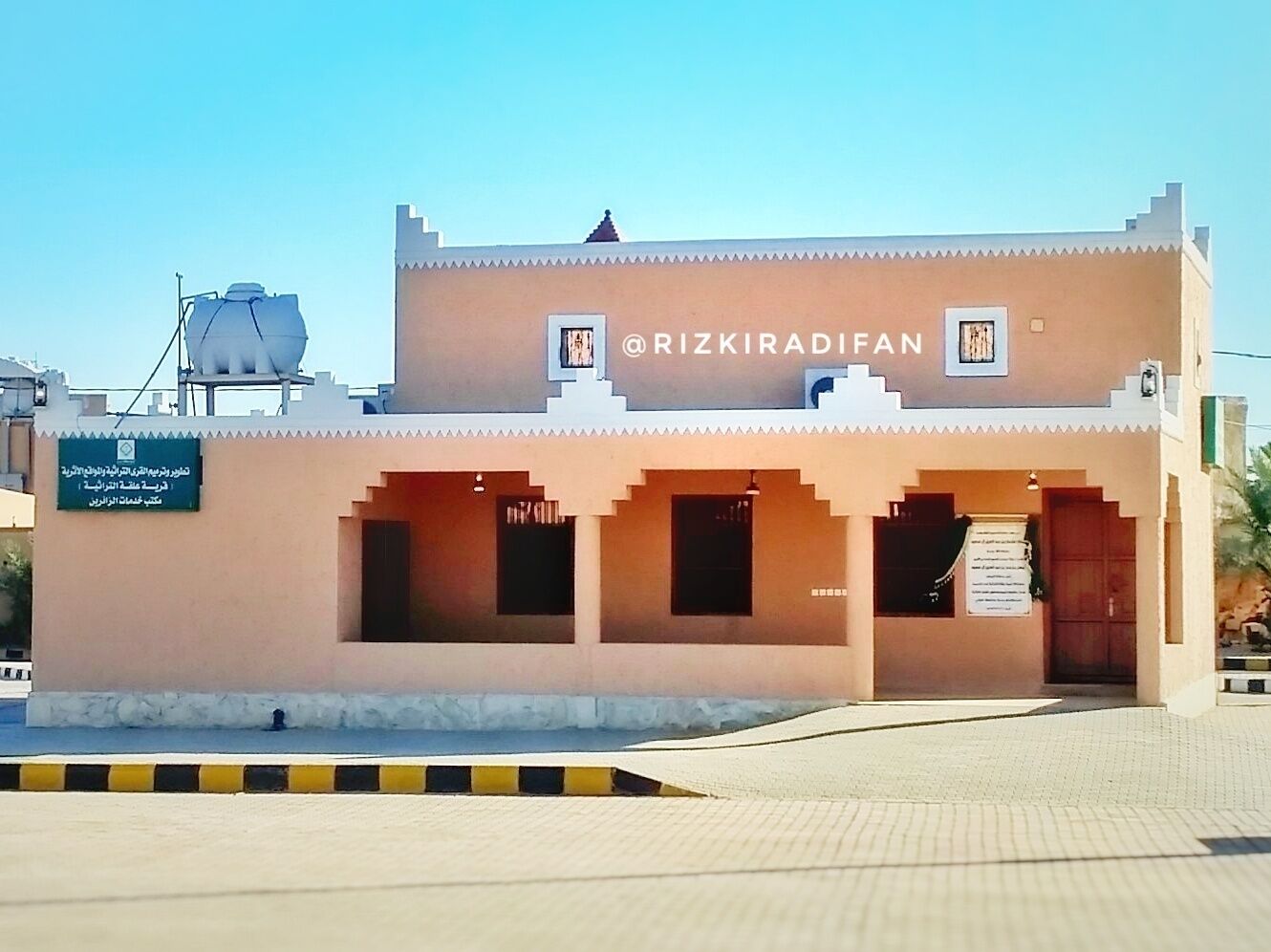A building with a sign reading "@RIZKIRADIFAN" and a signboard with text in a foreign language.
