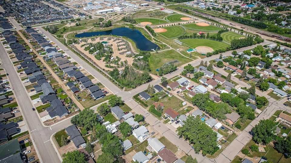 An aerial view of a residential area with houses, a baseball field, and a lake.