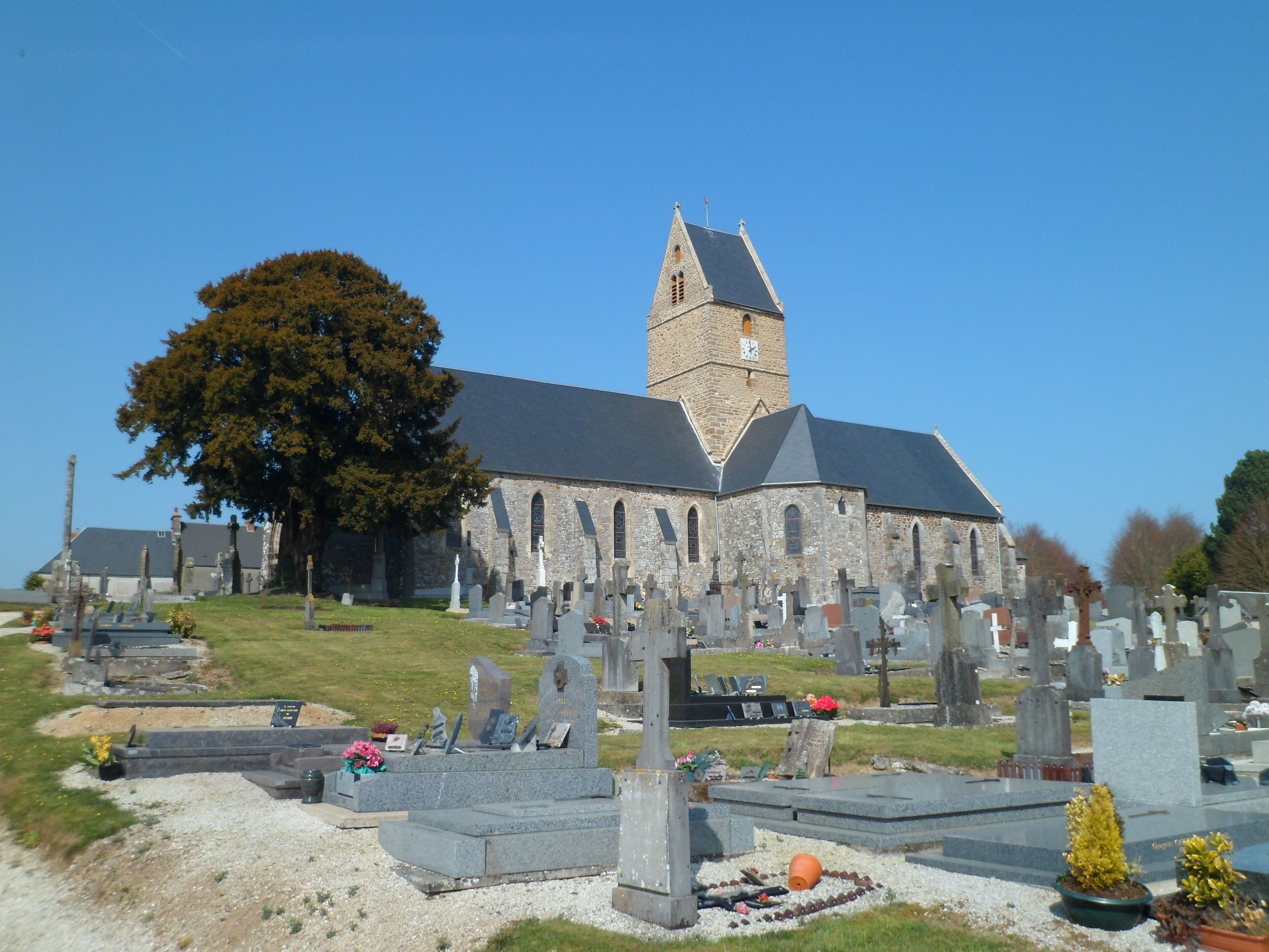 A church with a tall tower and a cemetery in front.