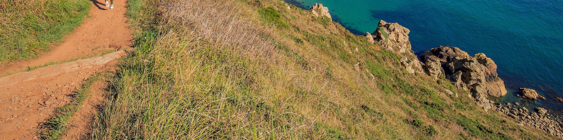 A coastal hiking trail with rocky cliffs and a clear blue sea.