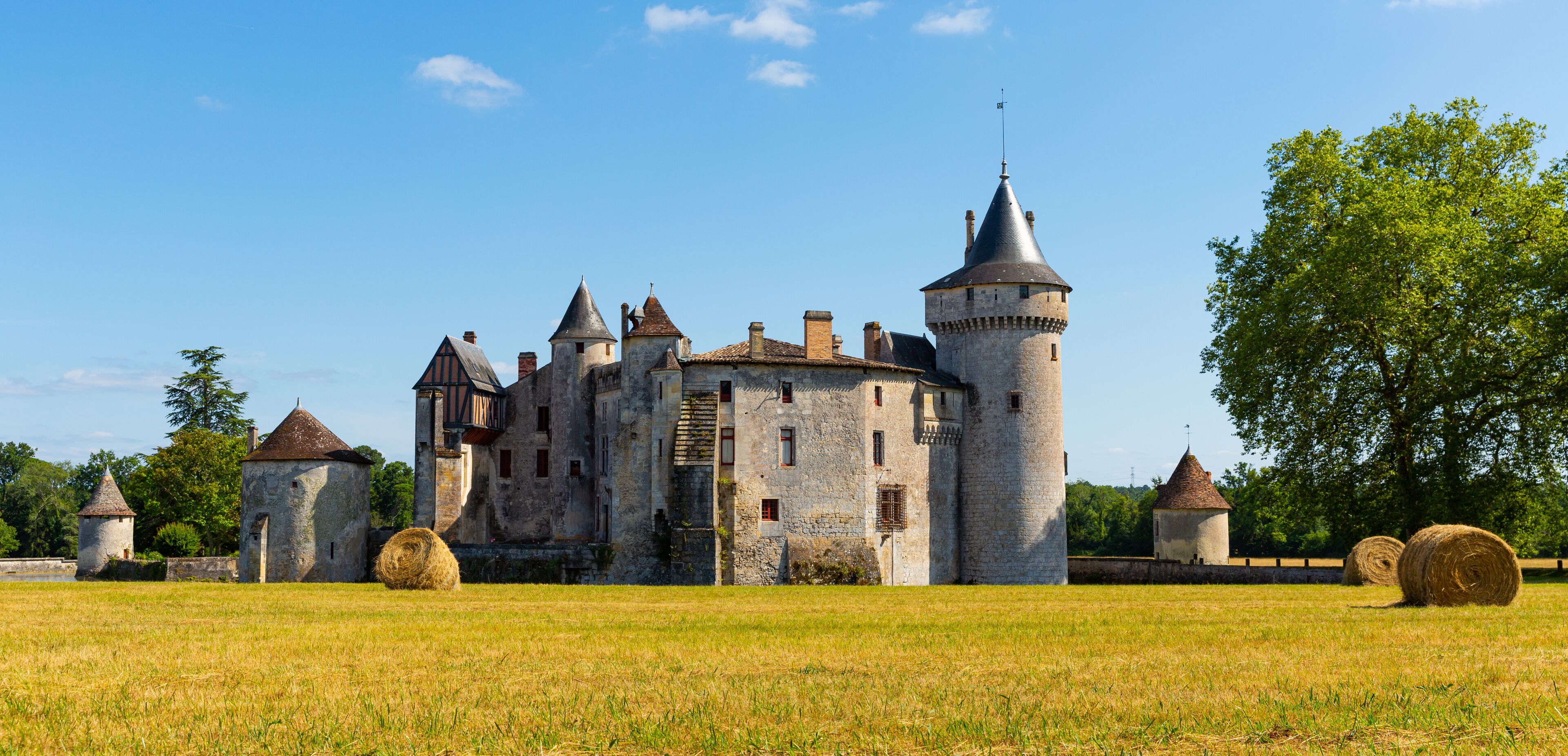 A medieval castle with multiple towers and a large field with hay bales.