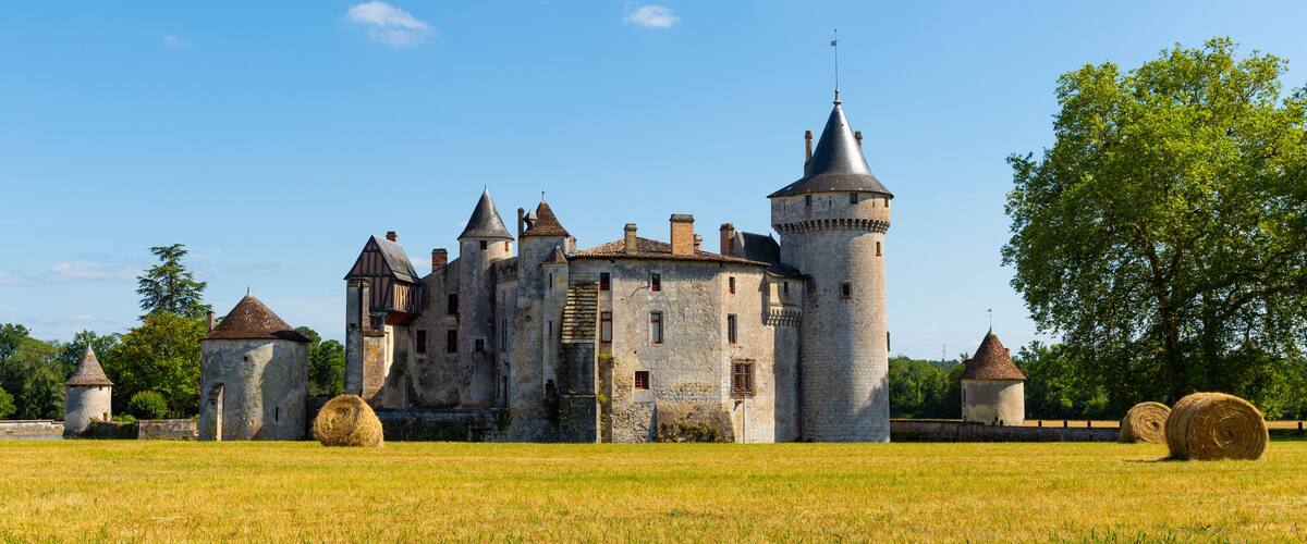 A medieval castle with multiple towers and a large field with hay bales.