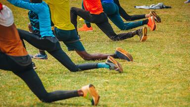 Stretching and warm-up of African runners. Joggers and marathon runners prepare to run on green grass. Photo from training in Kenya