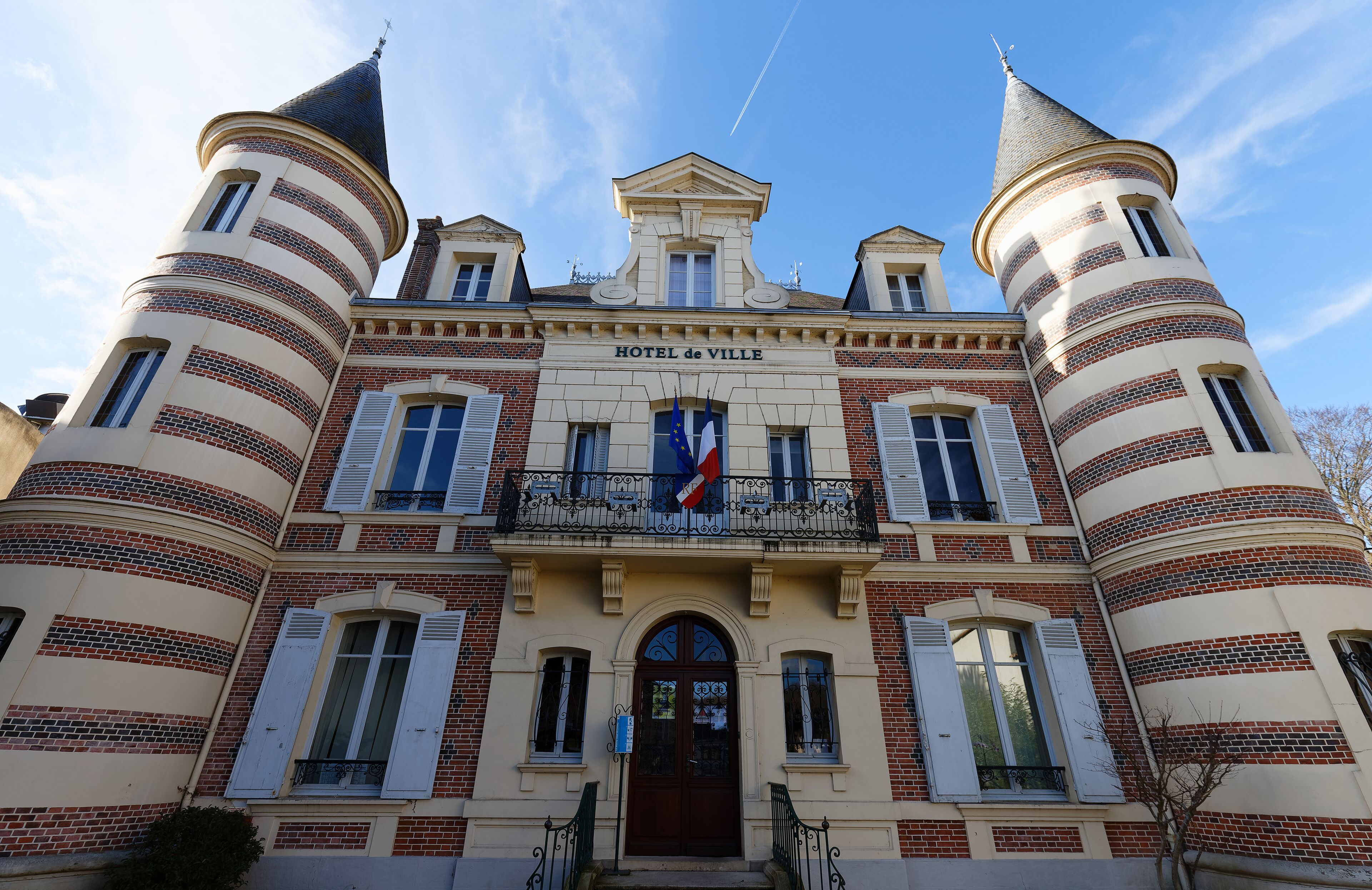 A historic building with a central entrance, two towers, and a balcony with flags.