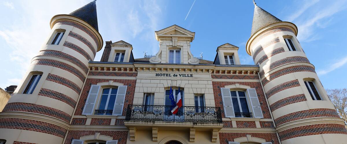 A historic building with a central entrance, two towers, and a balcony with flags.