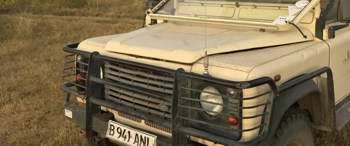 A white safari vehicle with a roof, parked in a grassy field.