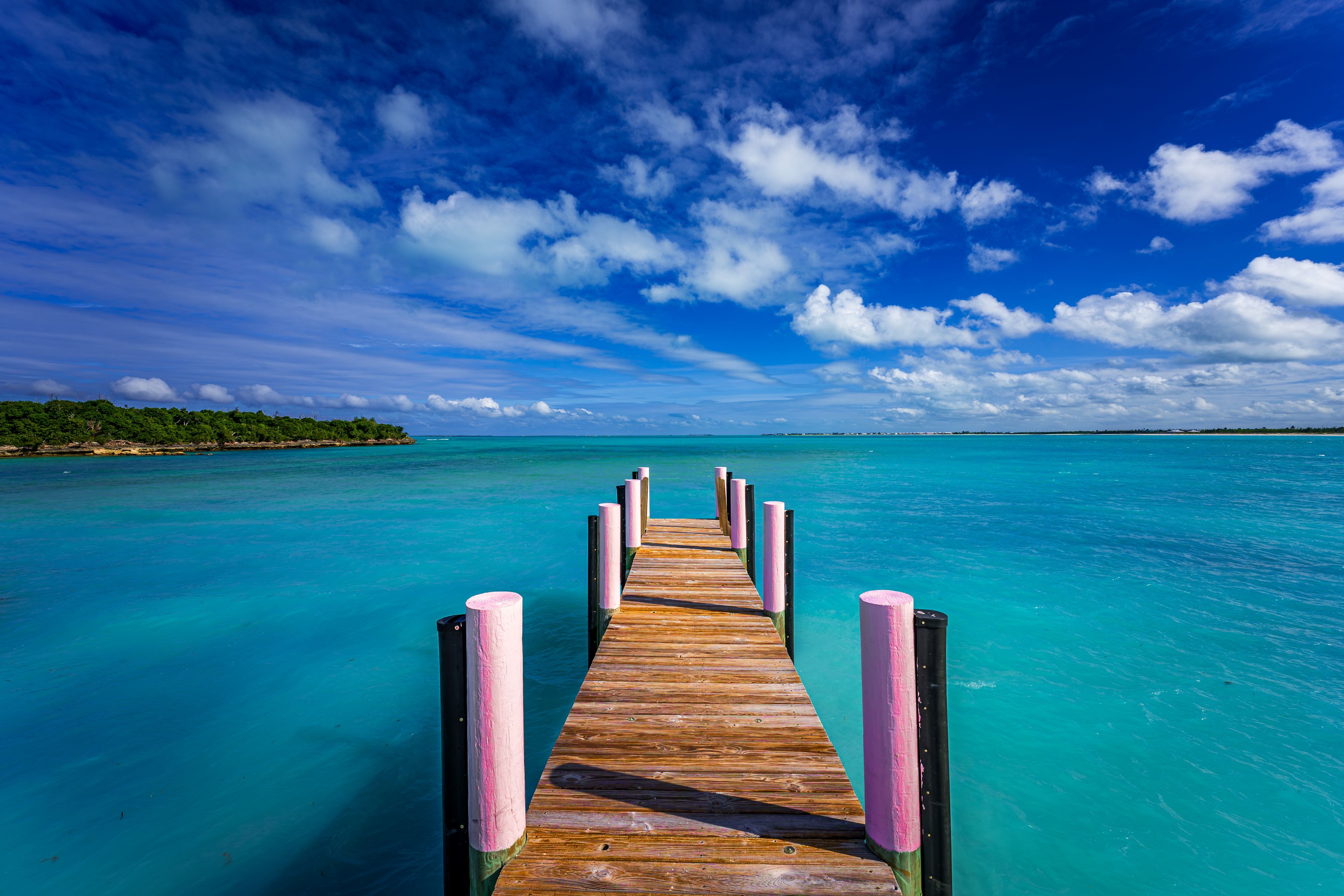 Wooden pier stretching into crystal-clear turquoise water under a dramatic cloud-filled sky at Casuarina Beach, Abaco, Bahamas - capturing the essence of tropical serenity and endless ocean views