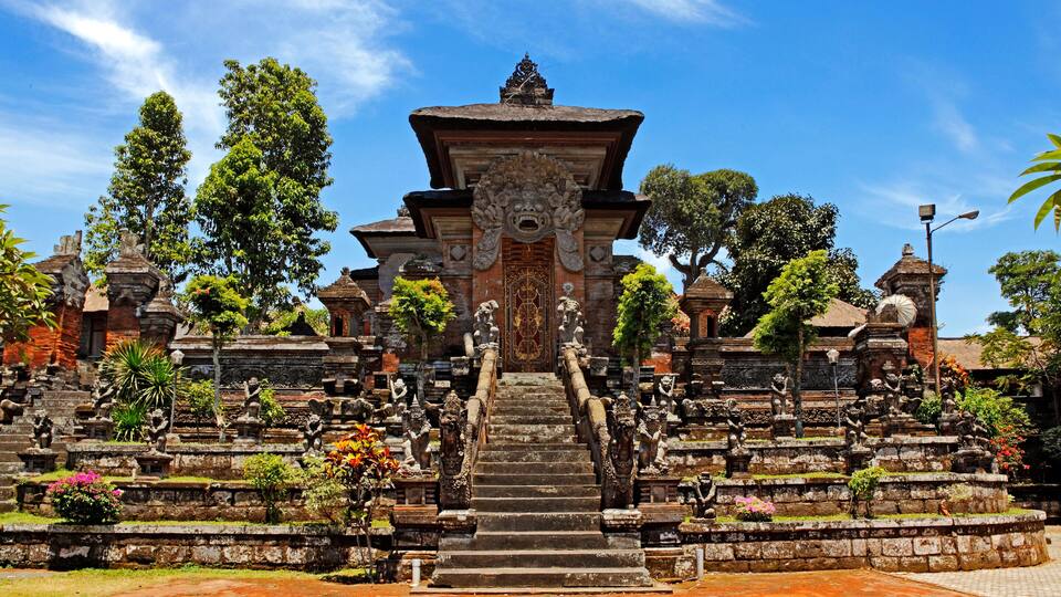 A temple with a central staircase, surrounded by stone statues and lush greenery.