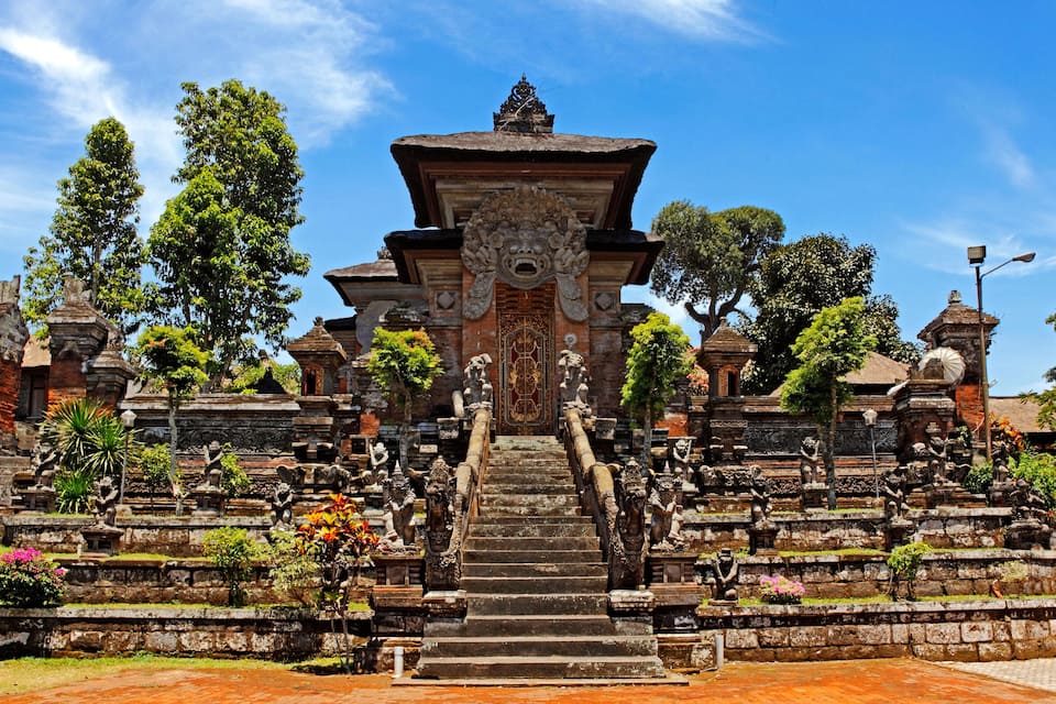 A temple with a central staircase, surrounded by stone statues and lush greenery.