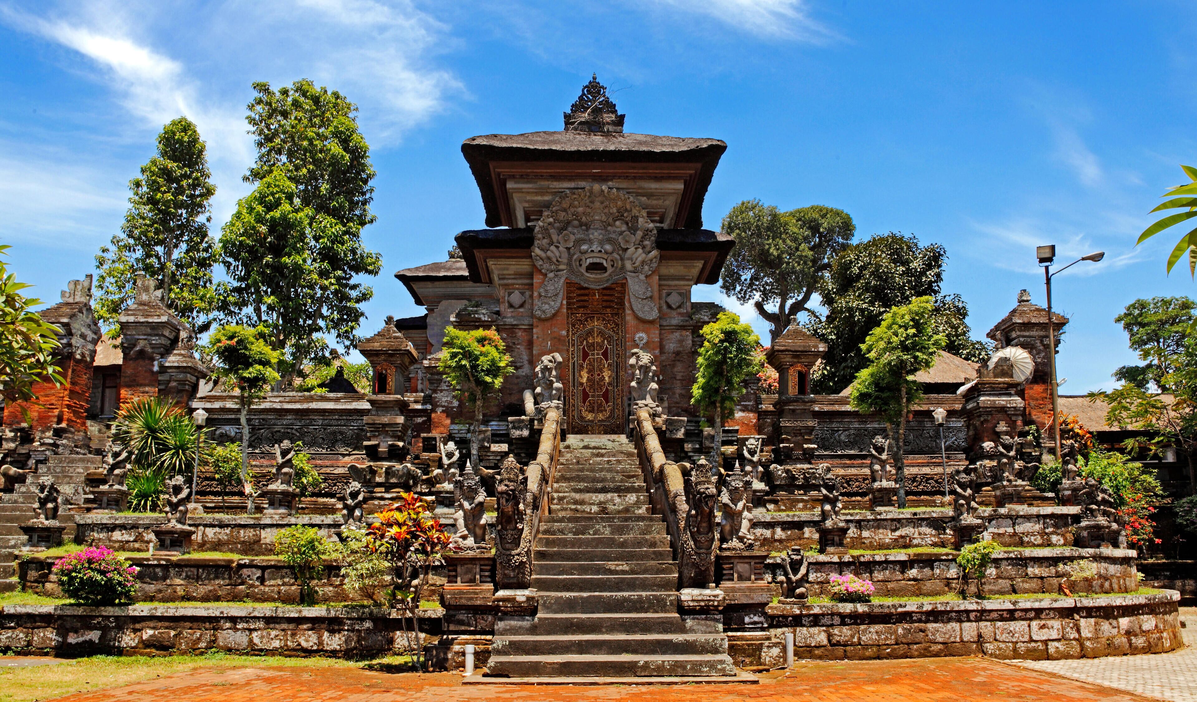 A temple with a central staircase, surrounded by stone statues and lush greenery.