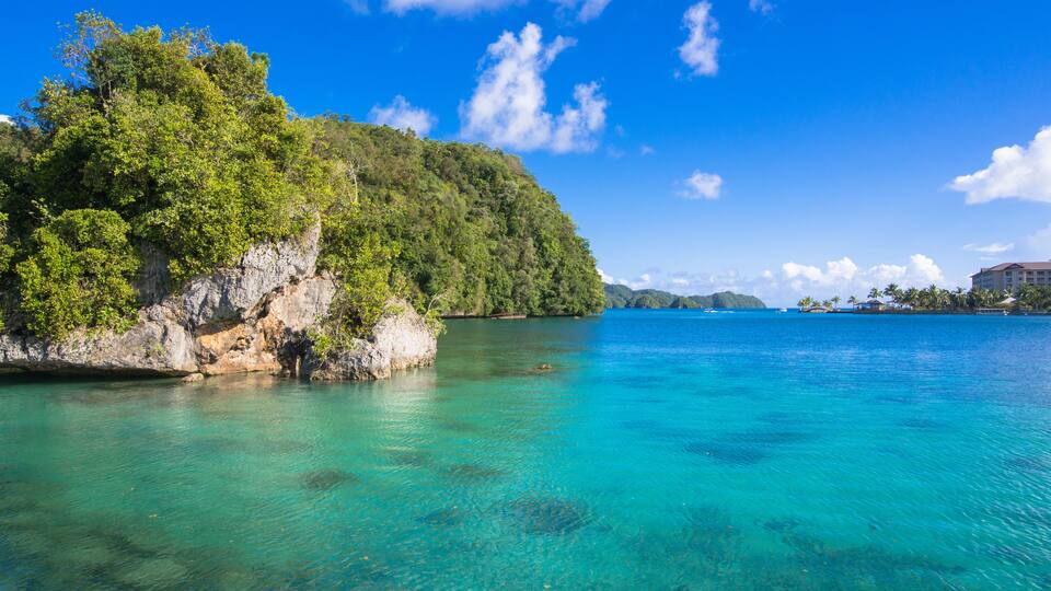 A clear turquoise sea, a rocky coastline, and a lush green hill.