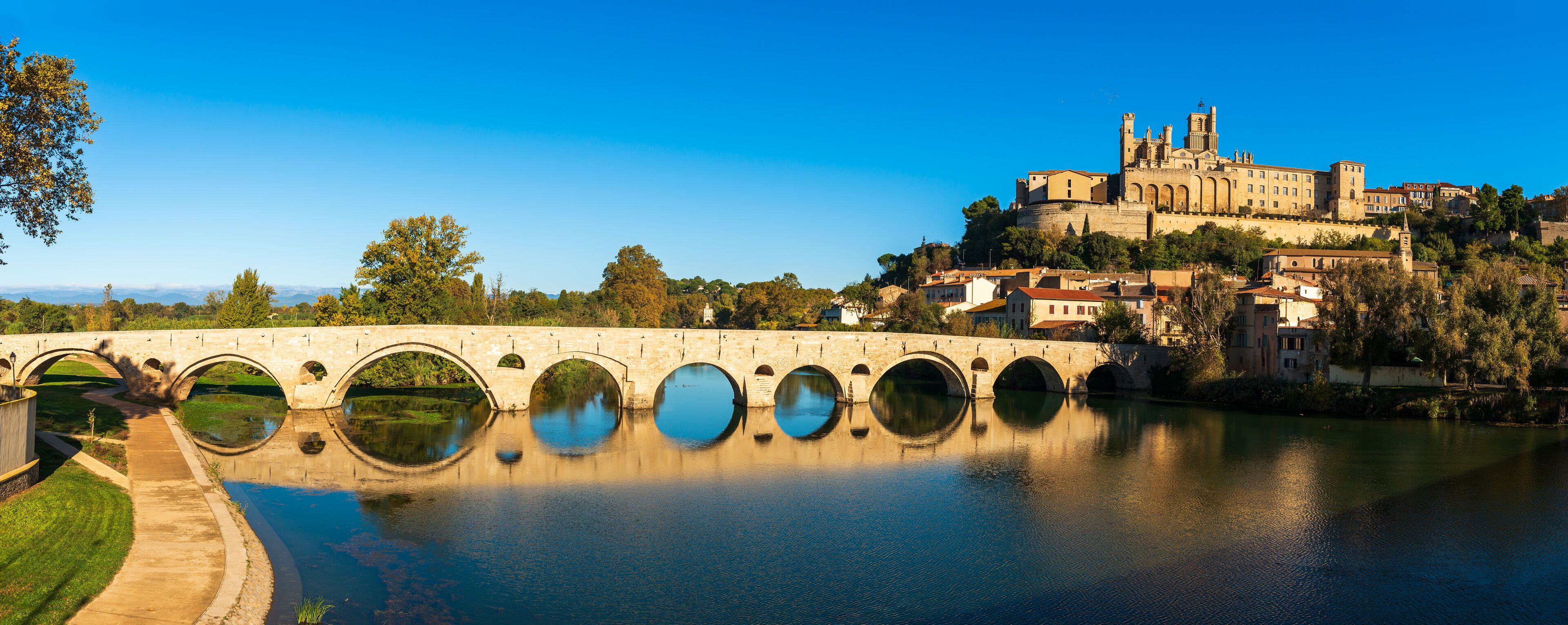 A stone bridge with multiple arches over a river, reflecting the surrounding buildings and trees.