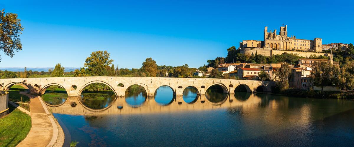 A stone bridge with multiple arches over a river, reflecting the surrounding buildings and trees.