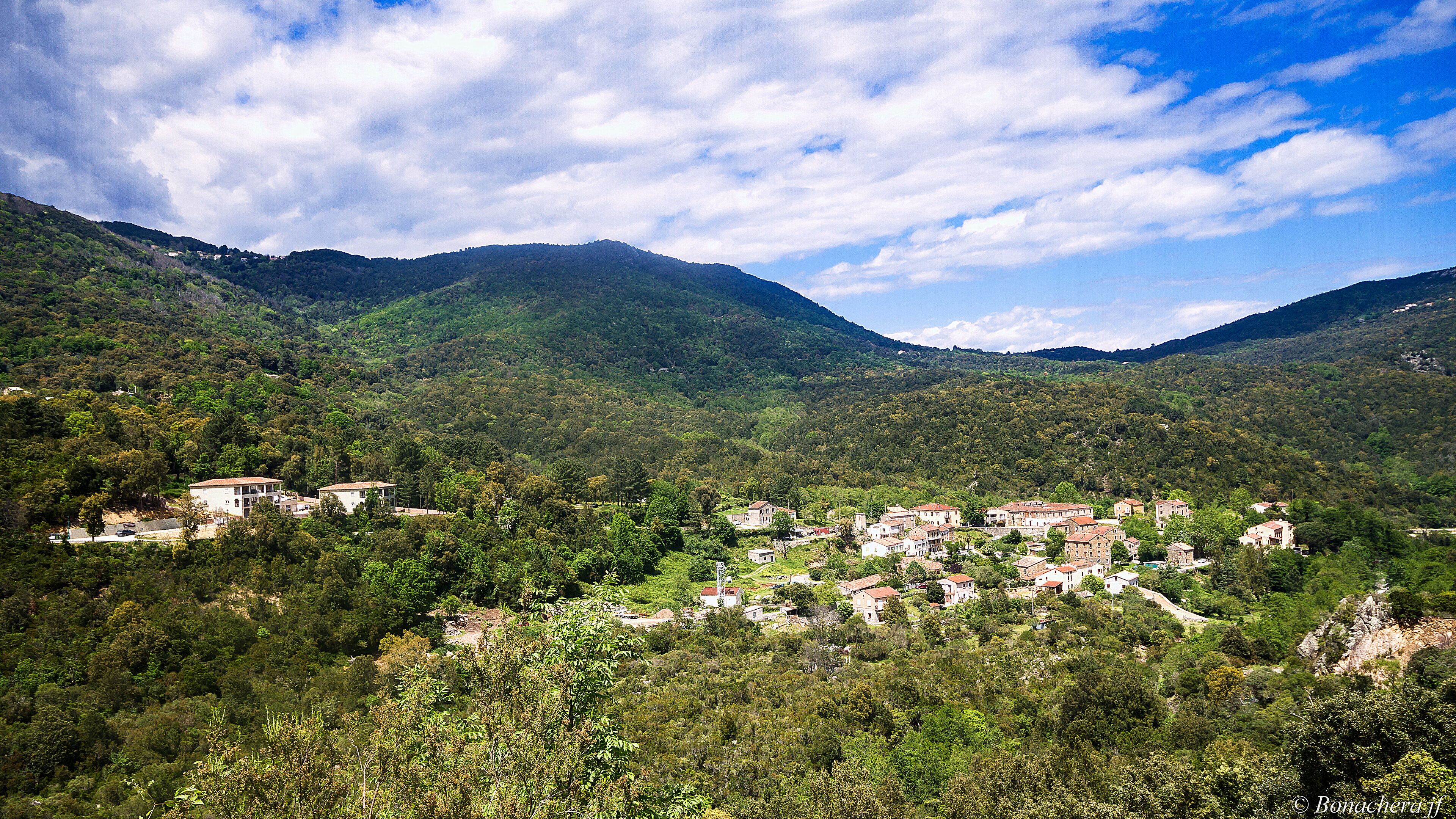 A village nestled in a valley surrounded by lush green hills and mountains.