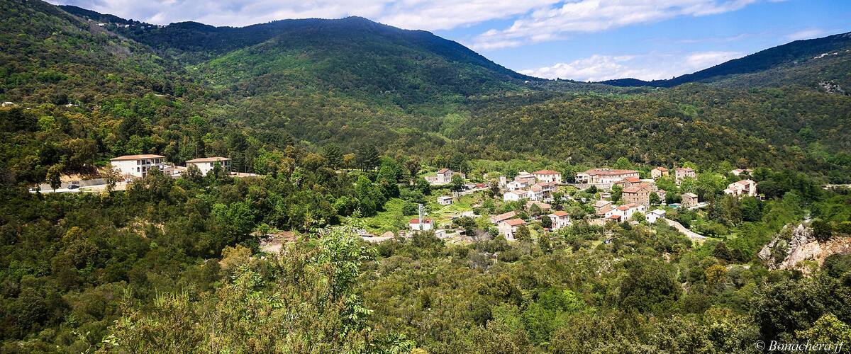 A village nestled in a valley surrounded by lush green hills and mountains.