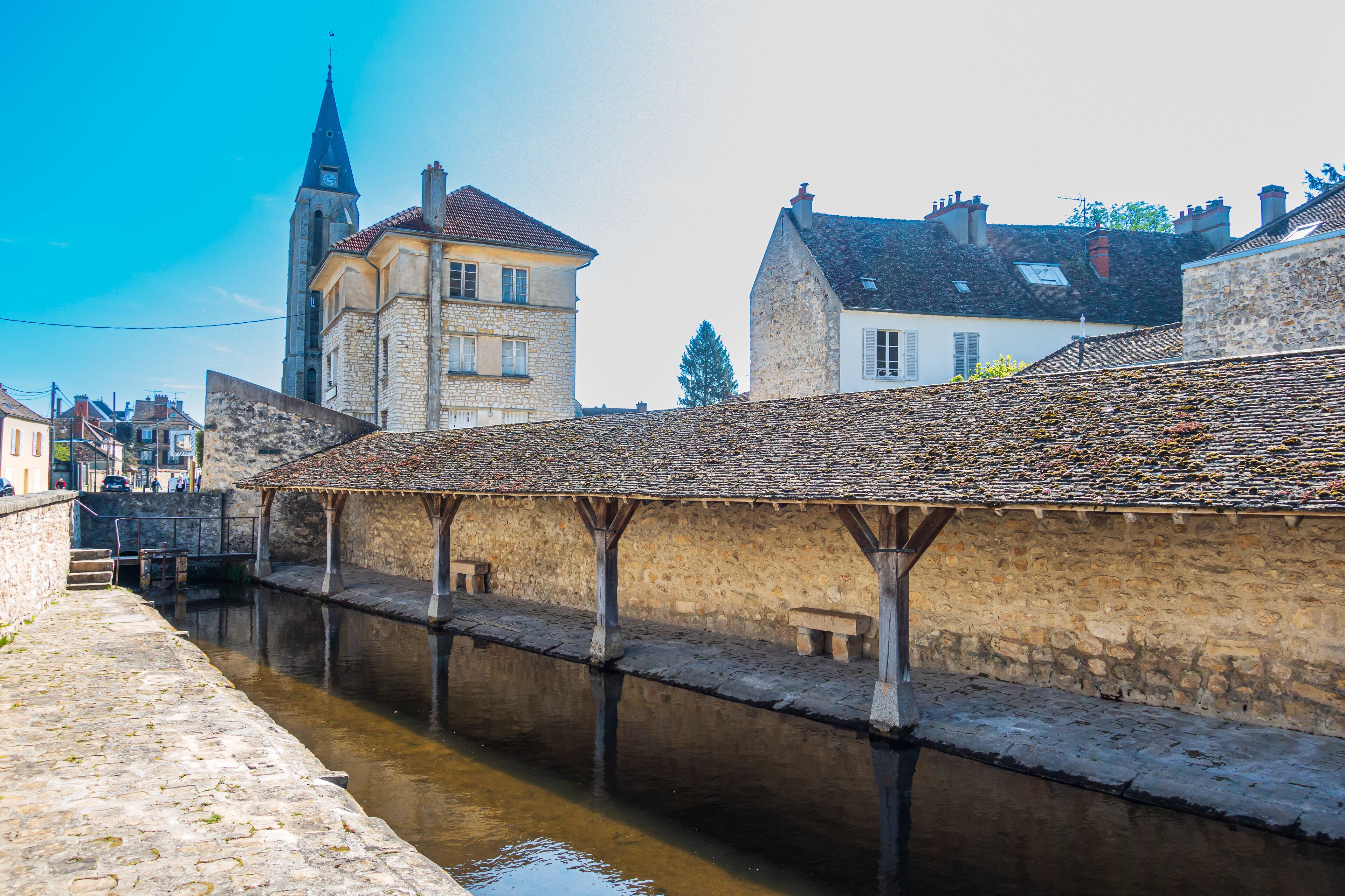 A stone bridge over a canal with a historic building and a church tower in the background.