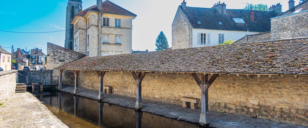 A stone bridge over a canal with a historic building and a church tower in the background.