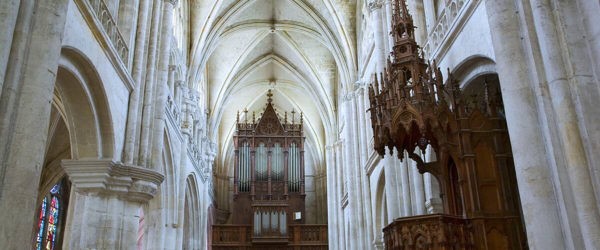 A cathedral interior with high vaulted ceilings, ornate wooden choir stalls, and a large organ.