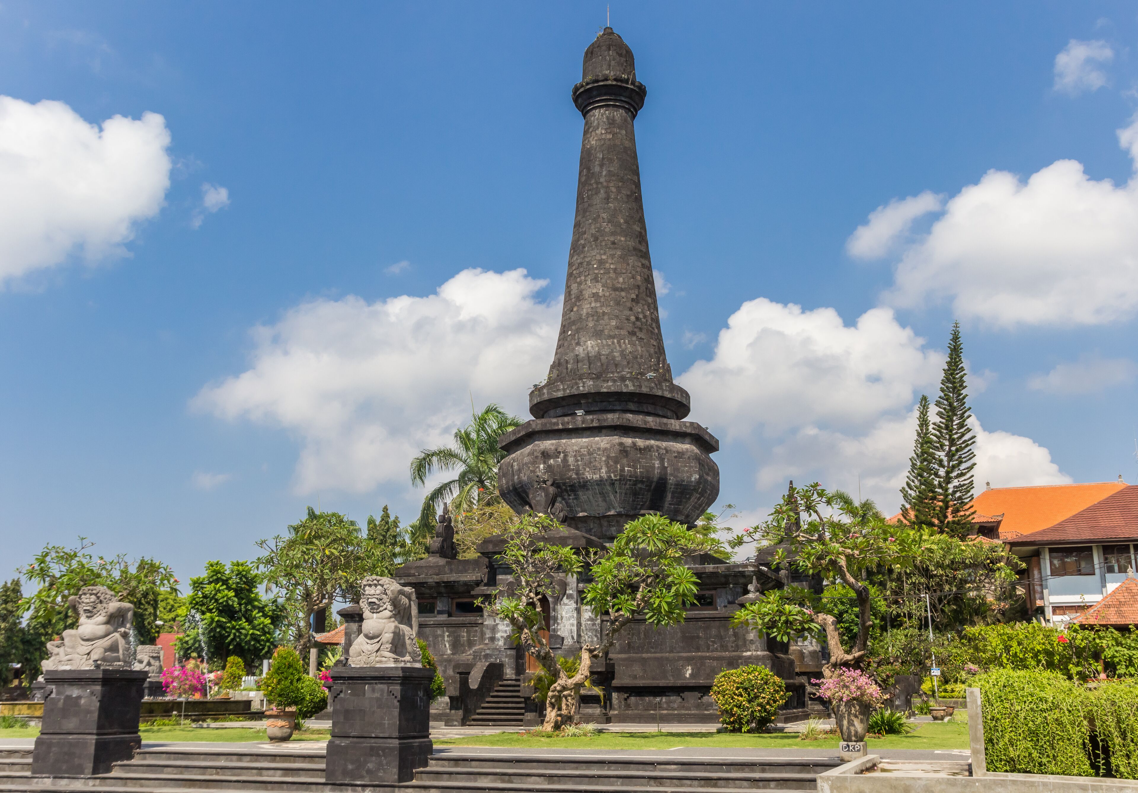 A tall stone monument surrounded by statues and lush greenery.
