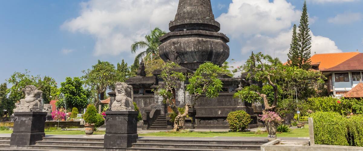 A tall stone monument surrounded by statues and lush greenery.