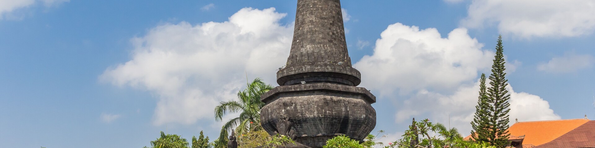 A tall stone monument surrounded by statues and lush greenery.