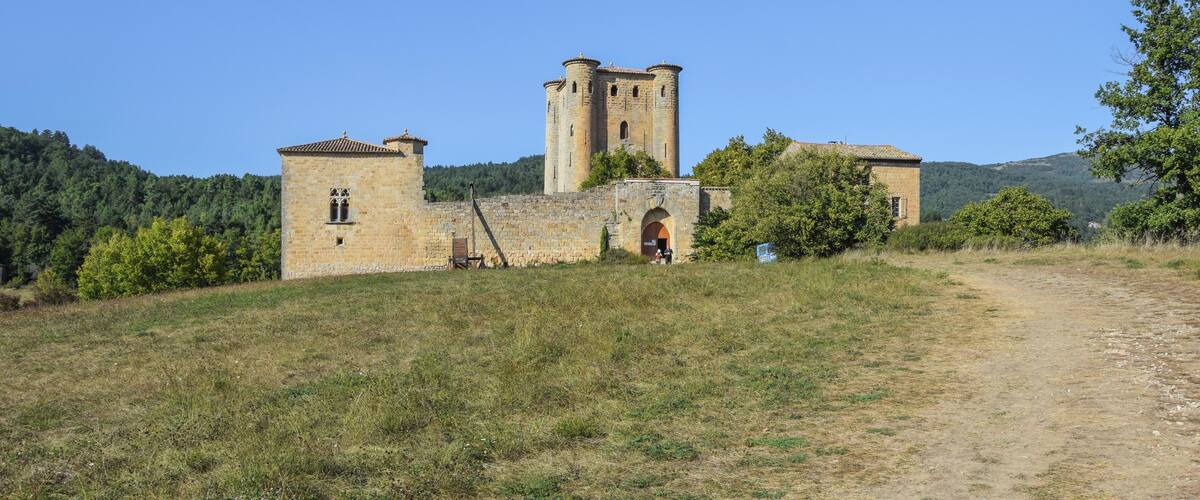 A historic stone building with a tower, surrounded by a grassy hill and trees.