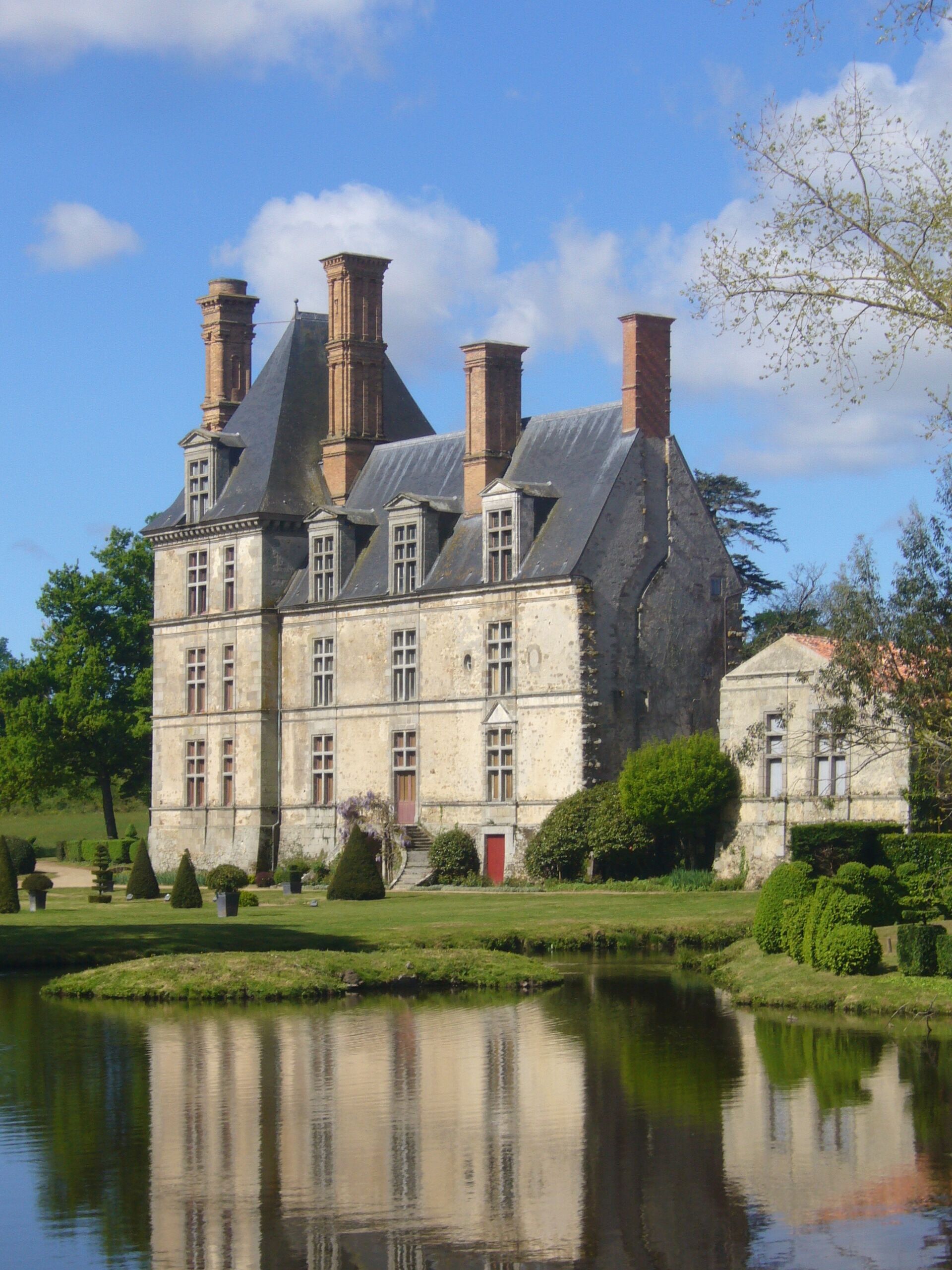 A large stone building with multiple chimneys and a pond in front.