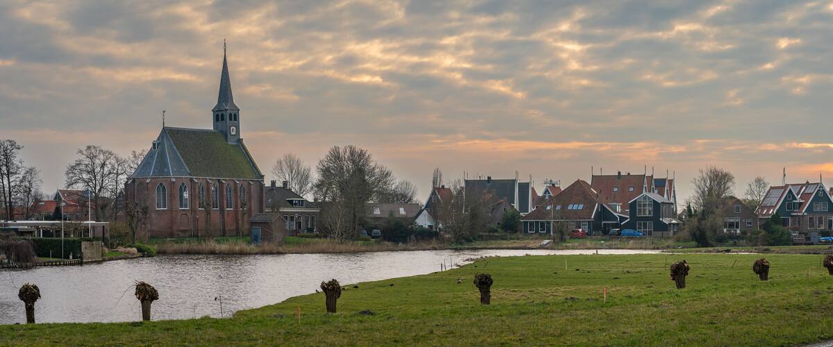 A riverside town with a church, houses, and a grassy field.