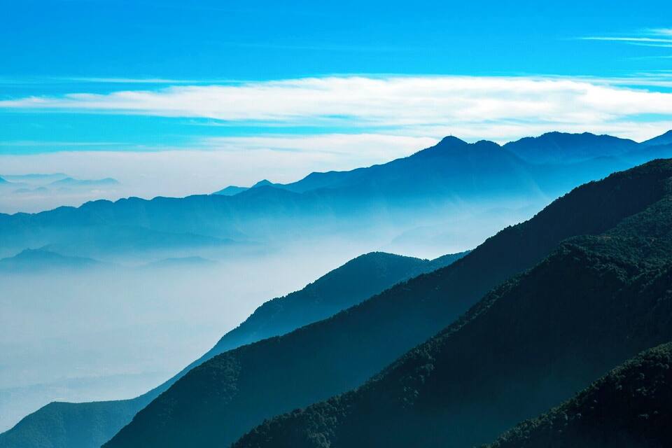 A mountain range with a clear blue sky and clouds at the base.
