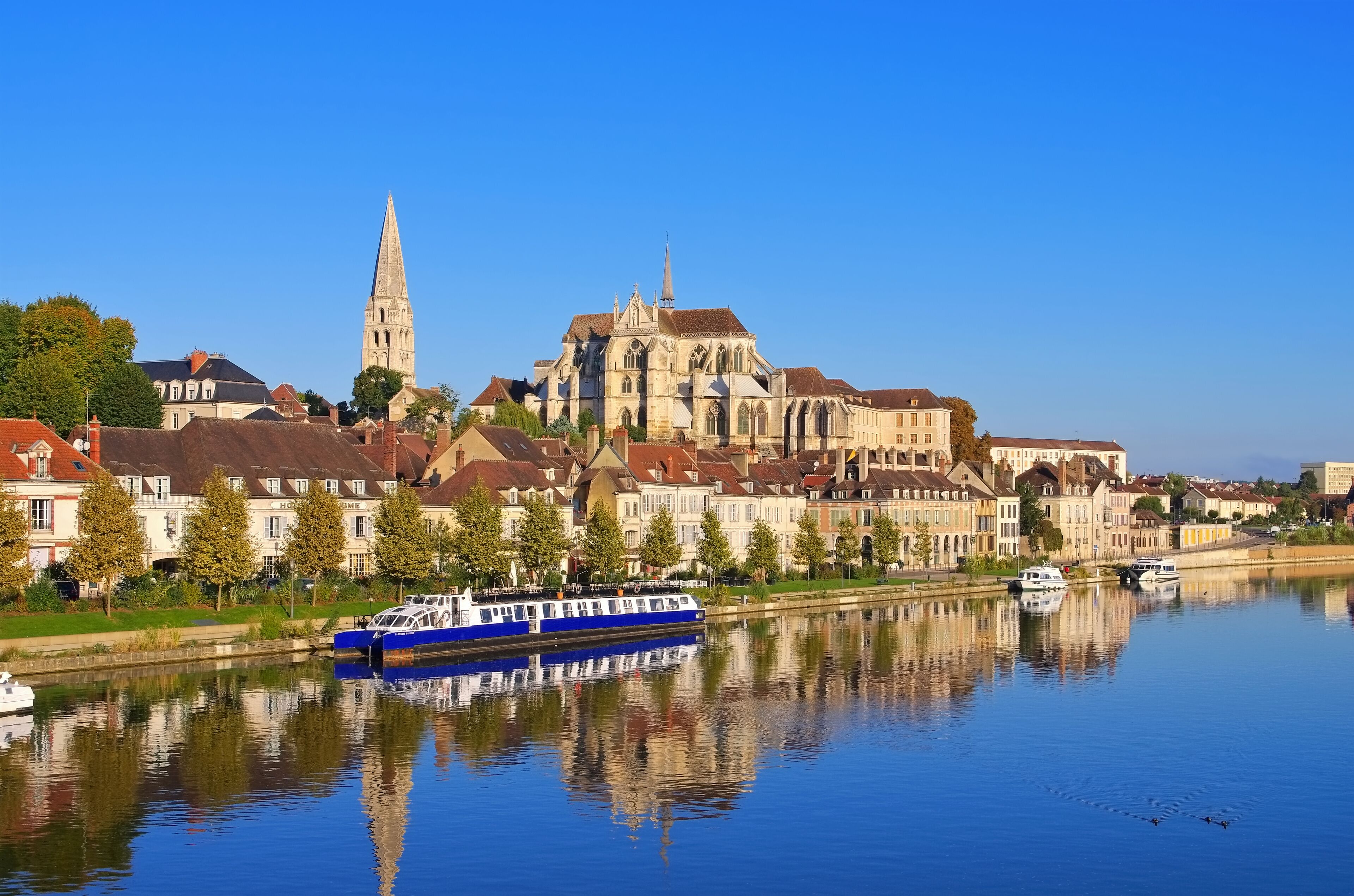 A river with a blue boat, a cathedral, and residential buildings along the riverbank.