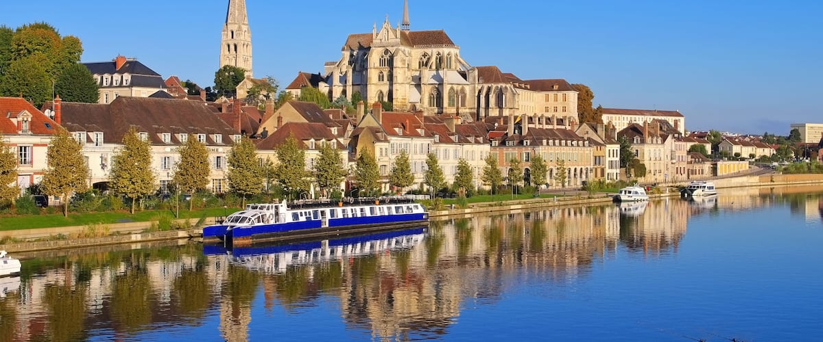 A river with a blue boat, a cathedral, and residential buildings along the riverbank.