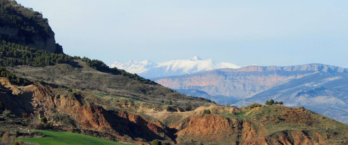 A mountainous landscape with green fields and snow-capped peaks in the distance.